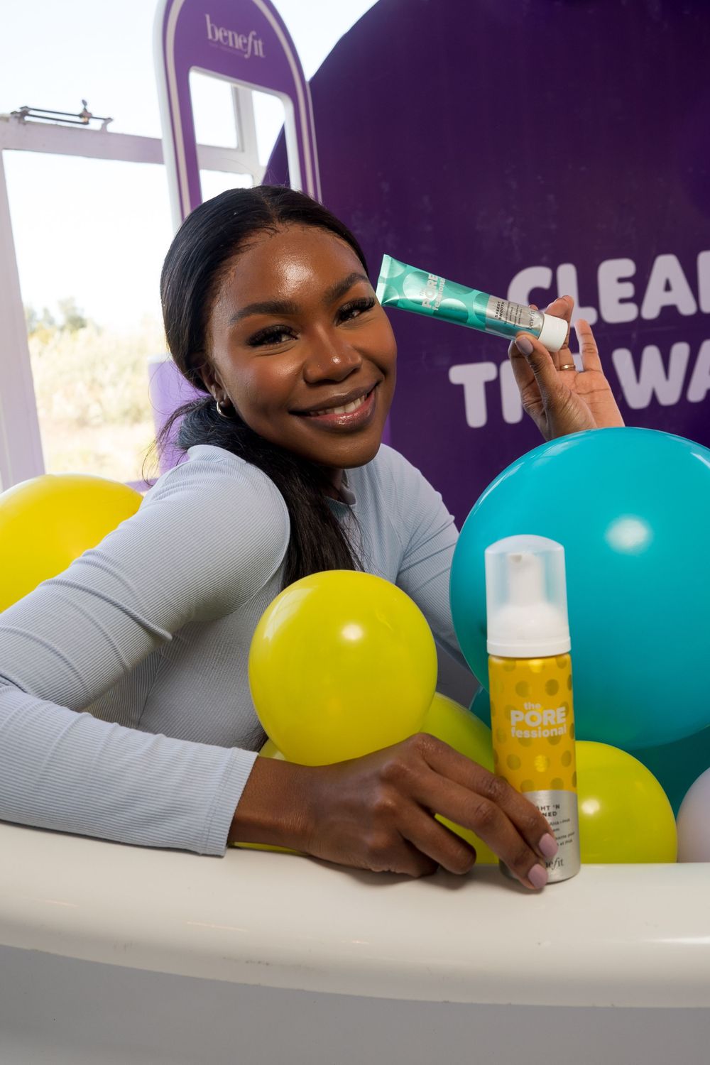 Product display with colorful balloons and skincare items against purple backdrop.