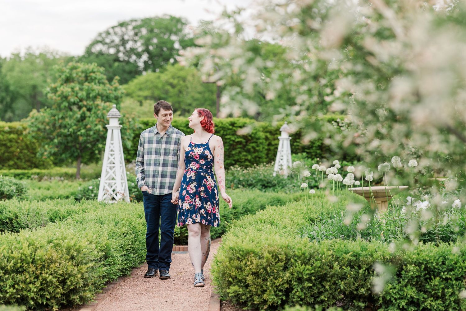 A couple walks hand in hand along a garden path surrounded by blooming flowers and white obelisks. at Cantigny Park