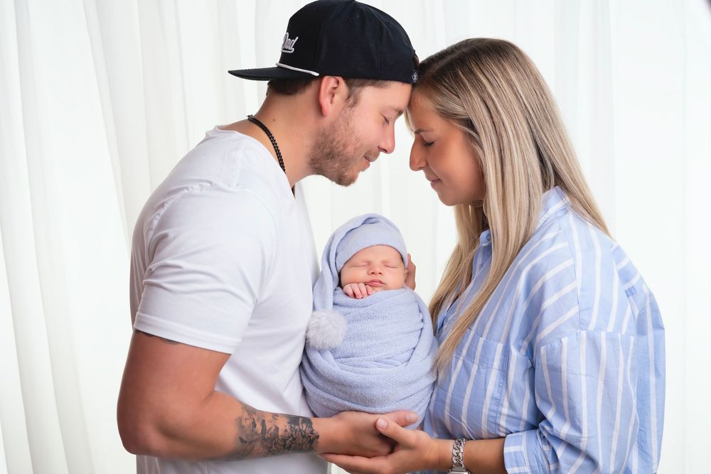 A couple holds and gazes lovingly at their newborn baby swaddled in a soft blue blanket.