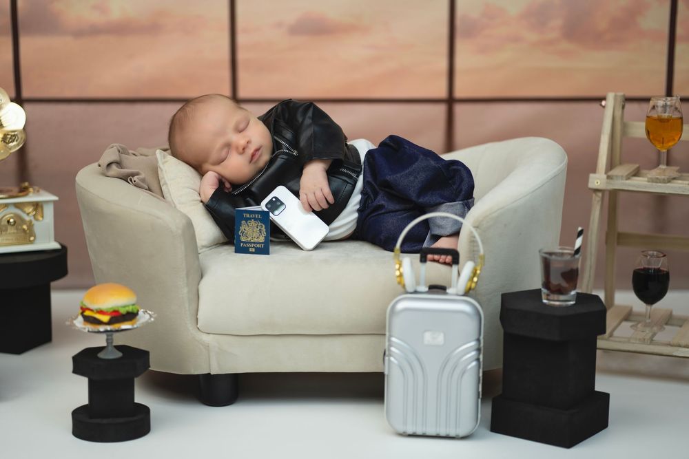 Small child sleeping on white couch with luggage and travel accessories in an airport lounge setting.