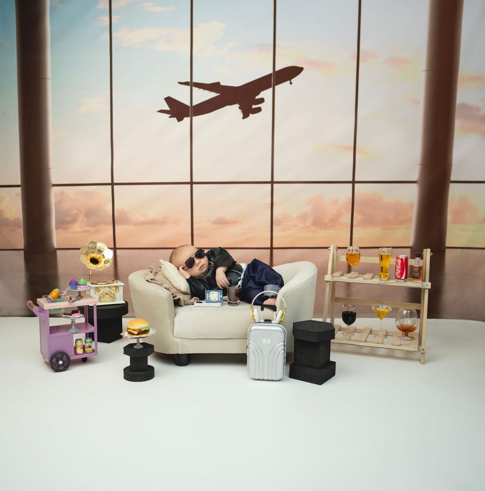 Airport lounge scene with miniature decor featuring a white couch, snack cart, and plane silhouette in window at sunset.