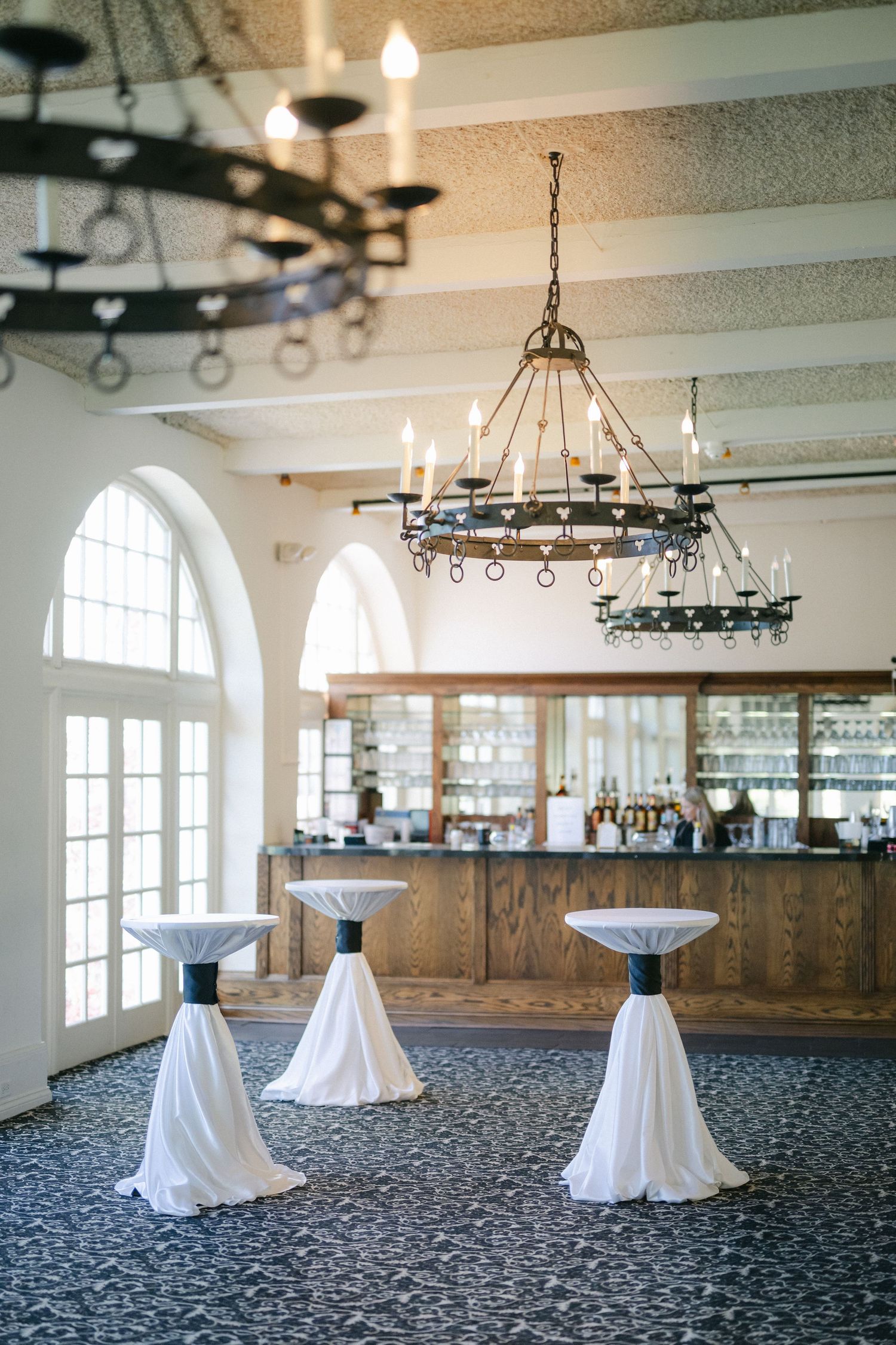 Elegant wedding reception table with white linens, black chiavari chairs and arched windows in bright white venue.