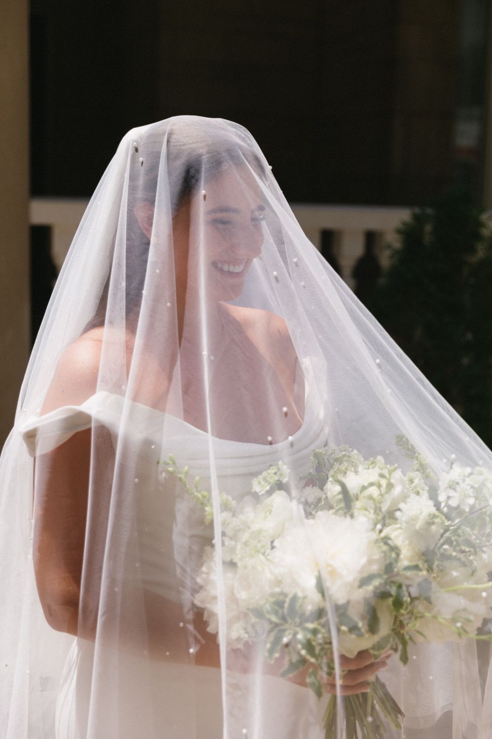A bride in a sheer white veil carries a classic bouquet of white flowers on her atlanta intimate wedding day at the wimbish house