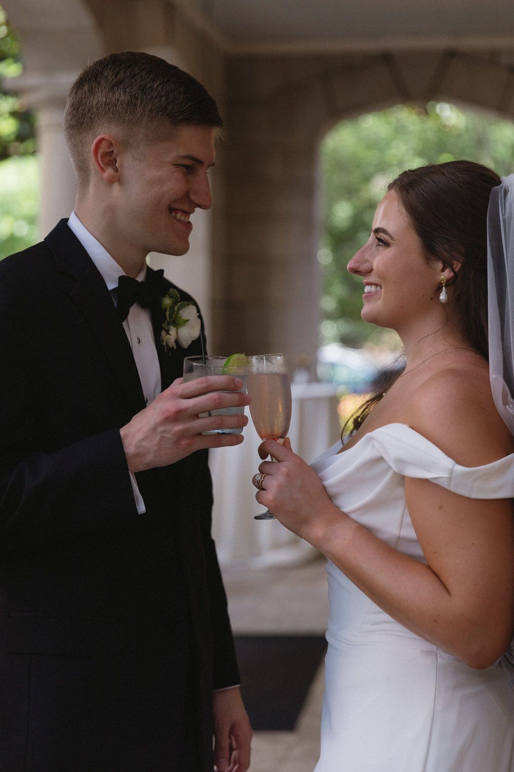 A bride in a white off-shoulder gown and groom in a black tuxedo share a toast during their intimate wedding celebration at wimbish house