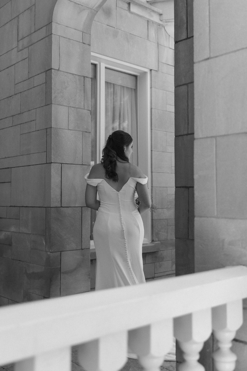 A black and white photograph of a bride in an elegant gown standing on the porch of the wimbish house on her atlanta elopement day