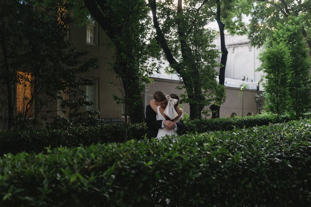 A couple dances together in a romantic garden setting at dusk, surrounded by lush hedges and trees on their elopement day