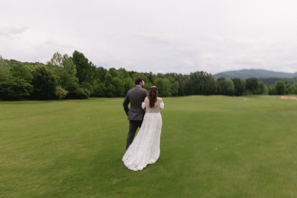 A couple in wedding attire stands together in a field in chattanooga with mountains in the background.