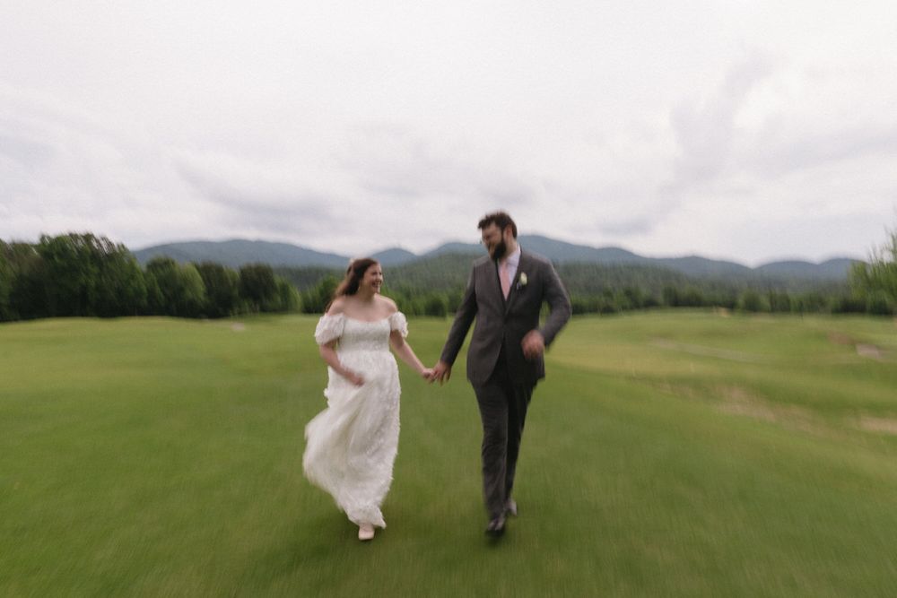 A couple runs hand in hand across a lush green field with mountains in the background on their chattanooga wedding day.