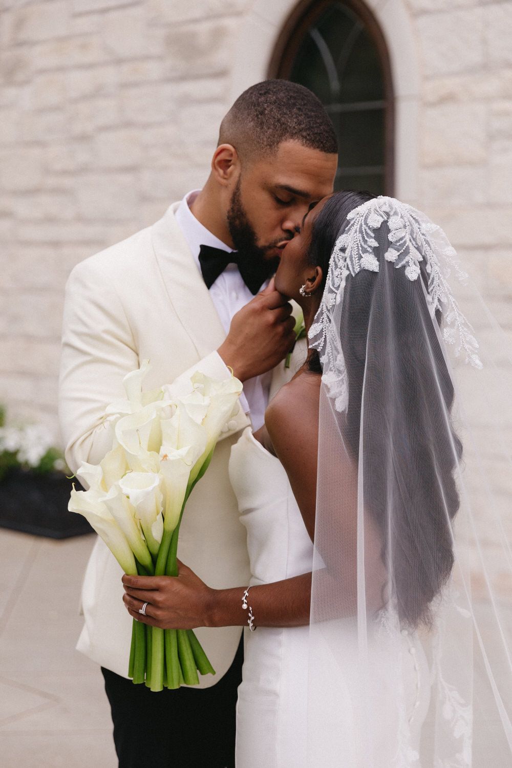 Elegant wedding couple sharing an intimate moment while holding a bouquet of white calla lilies.