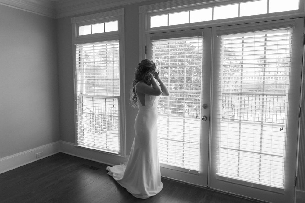 A figure in a flowing white wedding dress stands by french doors in a black and white photograph on her georgia airbnb wedding day