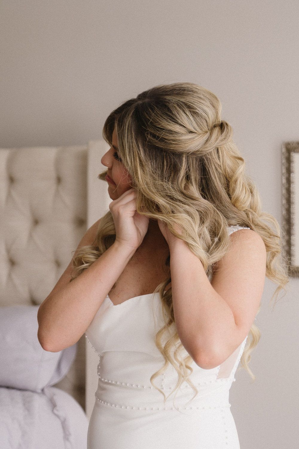 A bride wearing a white wedding dress adjusts her earring while getting ready for her elopement