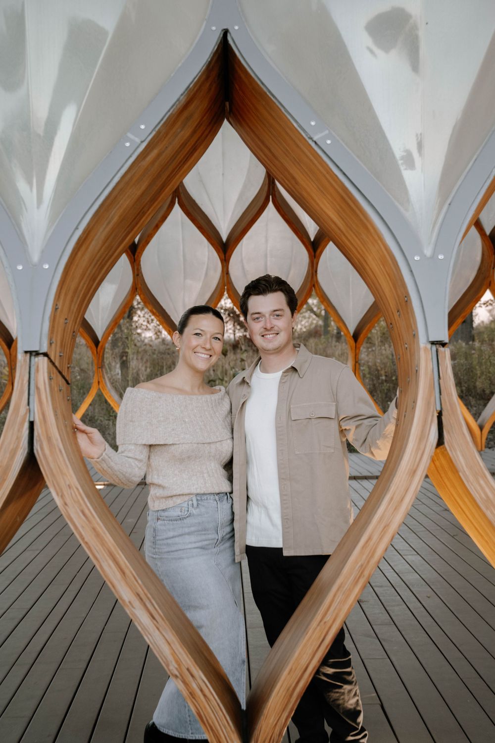 Couple standing together in an elegant wooden archway with gothic-inspired design elements and white vaulted ceiling.