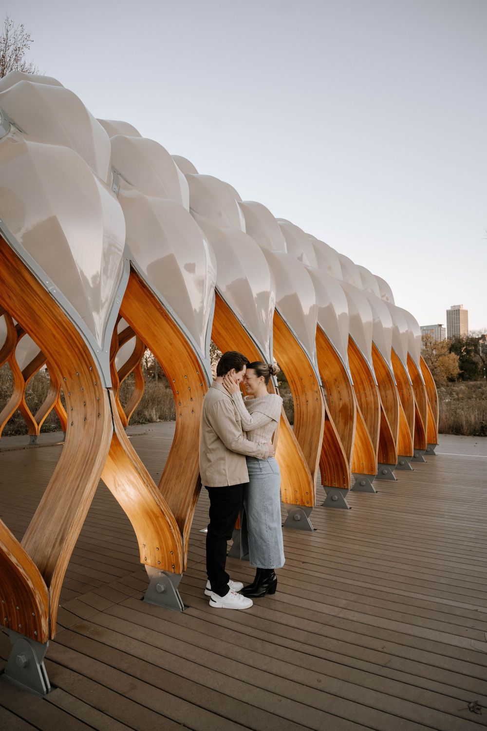 A couple stands intimately on a wooden boardwalk with unique curved architectural arches and white canopy overhead.
