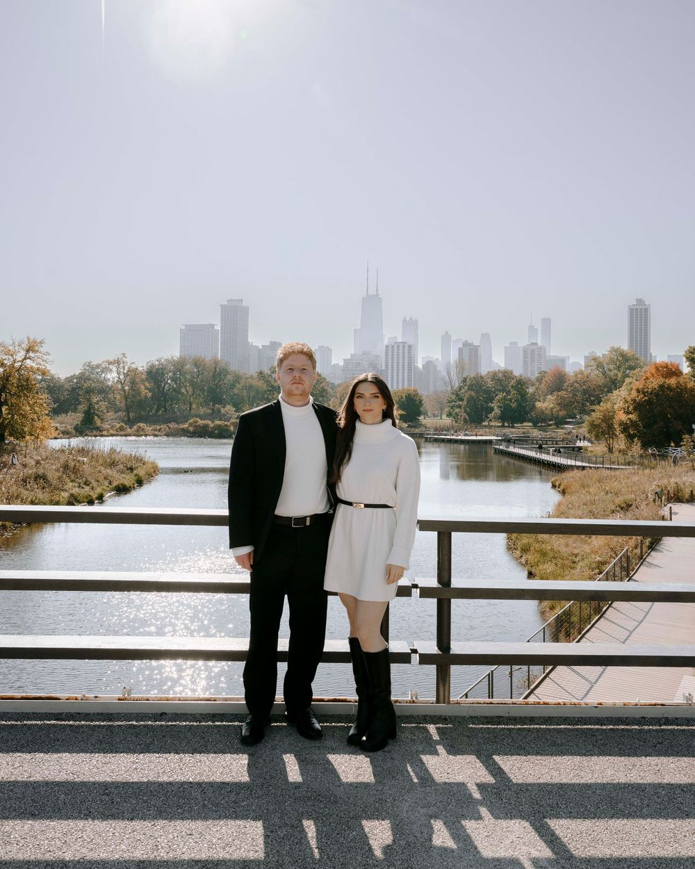 A couple poses on a bridge with the Chicago skyline visible in the background on an autumn day.