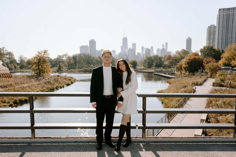A couple poses on a bridge in Lincoln Park with the Chicago skyline visible in the autumn background.