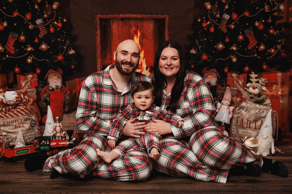 A cozy holiday family photo featuring matching plaid pajamas in front of a Christmas tree with presents and decor.