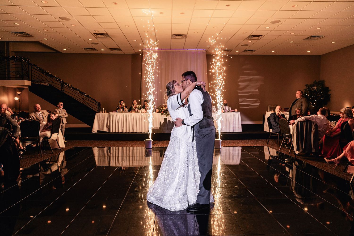 Couple shares their first dance as newlyweds on a reflective black dance floor with illuminated columns in the background.