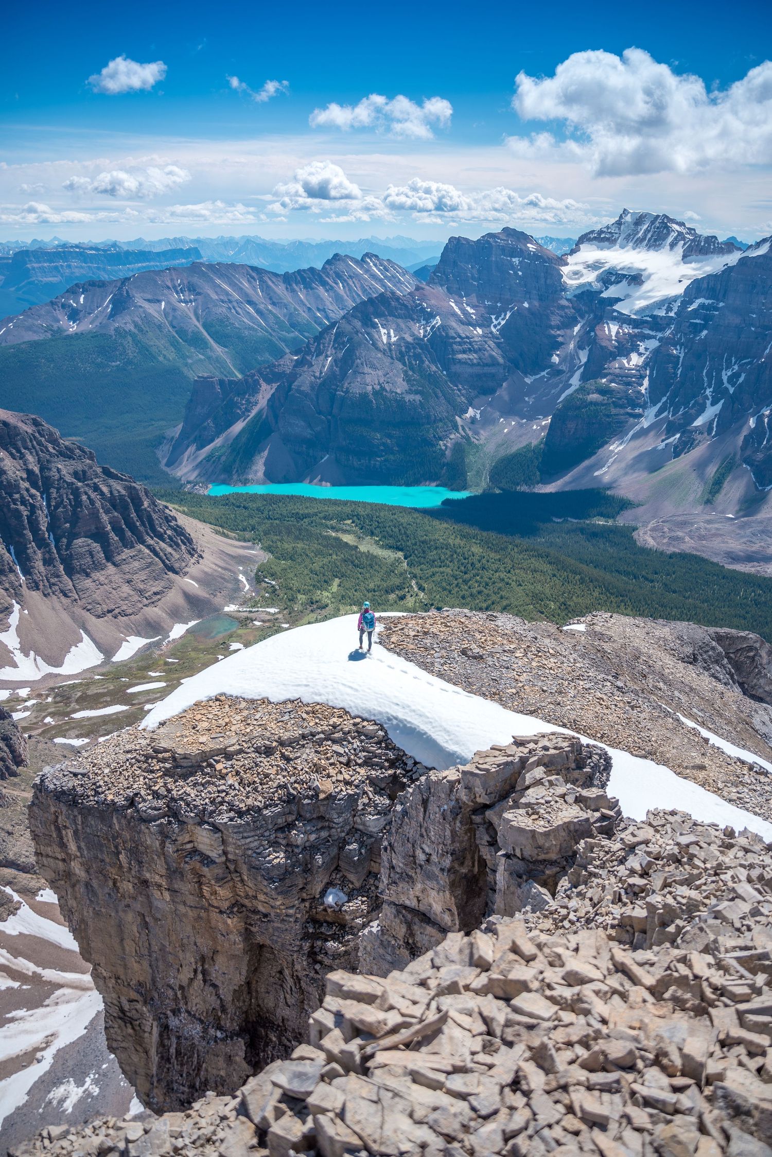 Stunning aerial view of turquoise Moraine Lake surrounded by Rocky Mountain peaks with snow patch in foreground.