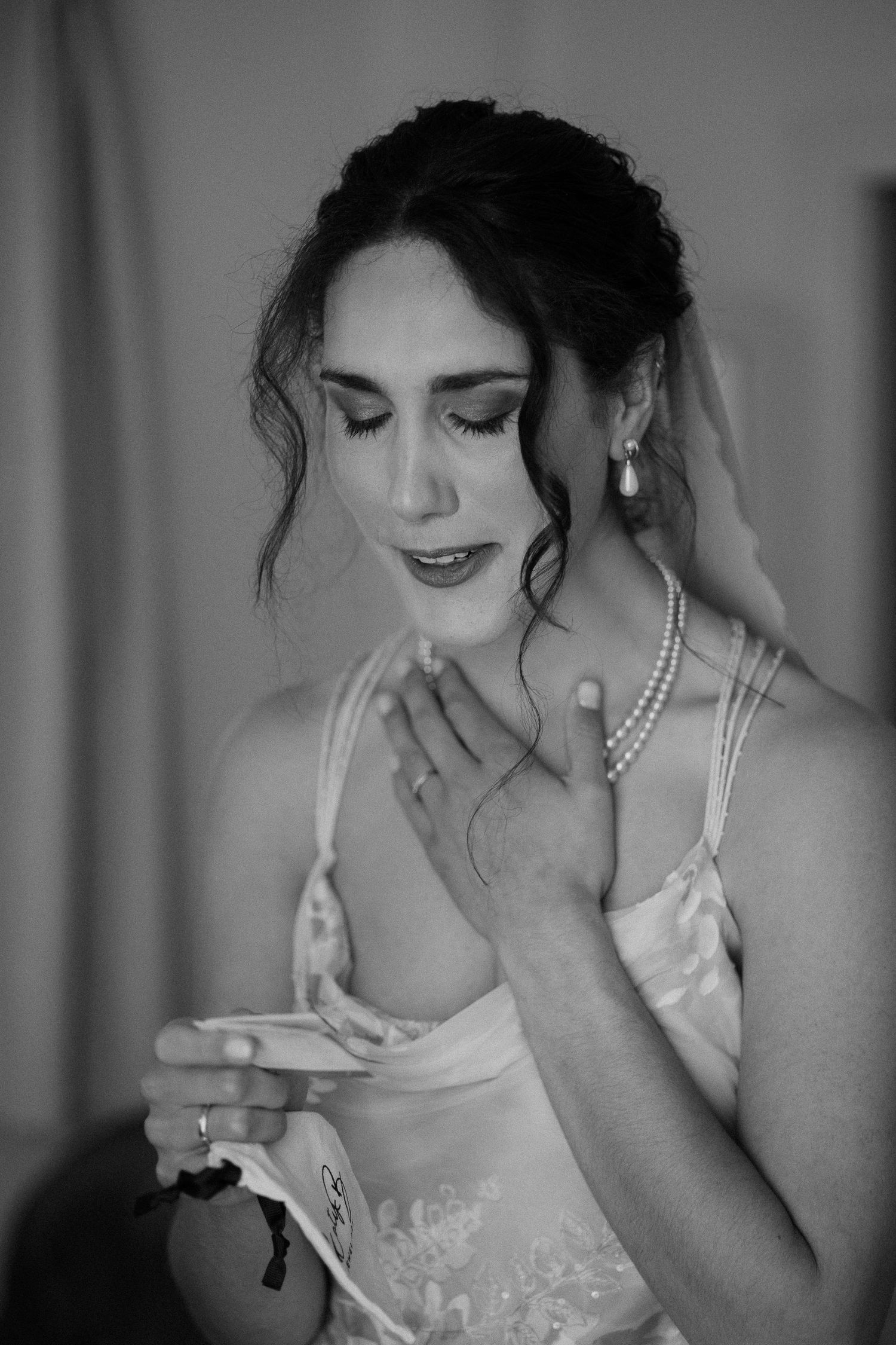 Black and white portrait of a bride wearing a lace gown and pearl necklace, with upswept hair and closed eyes.