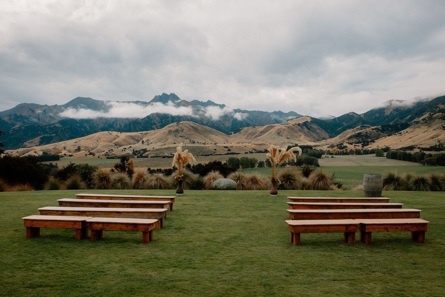 Wooden lounge furniture arranged on a green lawn beside a rustic green barn under autumn trees with colorful foliage.