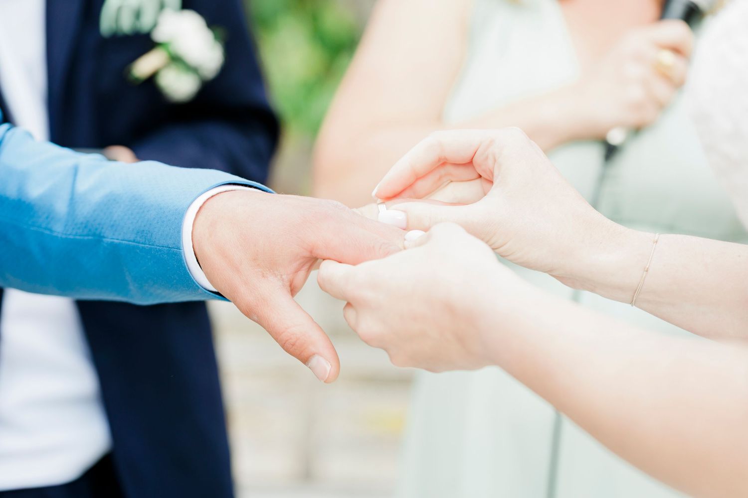 Close-up of hands exchanging rings during outdoor wedding ceremony.