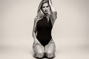 Woman in black one-piece swimsuit kneeling in artistic black and white studio photograph.