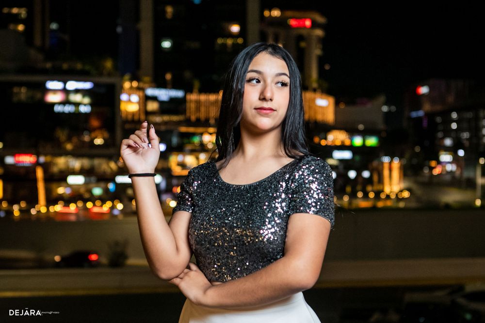 Person in outfit with white skirt poses on deck surrounded by decorative string lights at night.