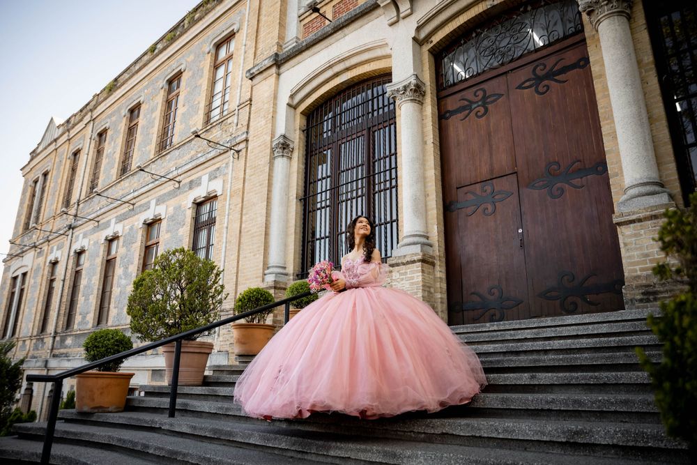 A pink ball gown sparkles on the historic stone steps of a grand building with ornate doors.