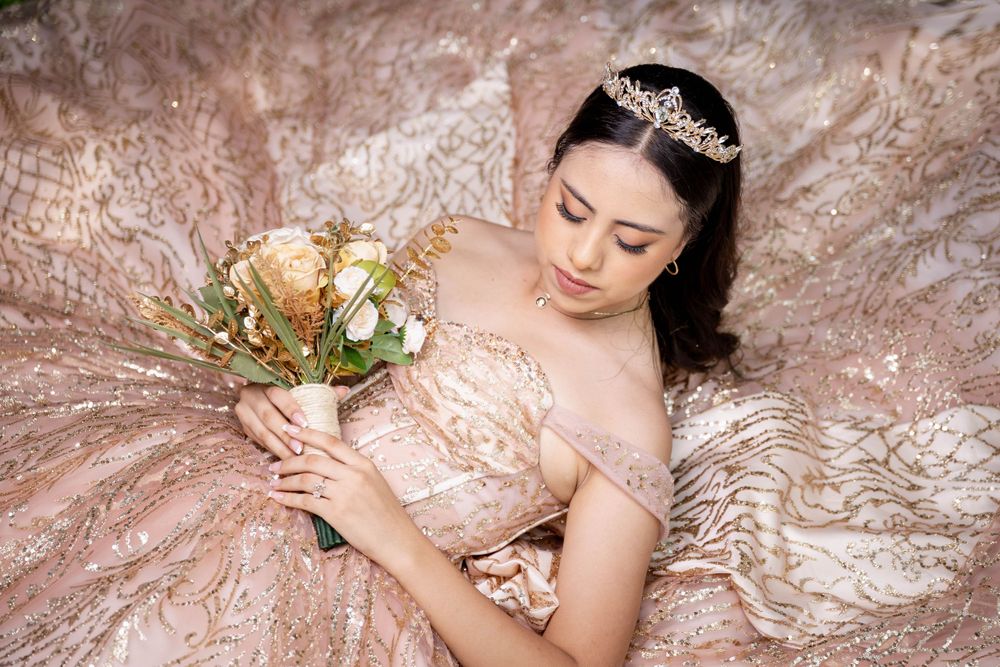 An elegant pink dress adorned with floral details and crystals is displayed with a matching bouquet.