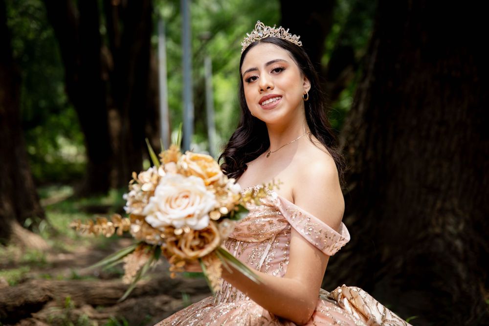 A shimmering champagne-colored quinceañera dress is showcased in a natural outdoor setting.