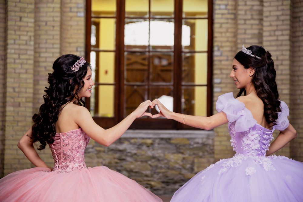 Two formal dresses in pink and purple shown in playful pose outside historic building.
