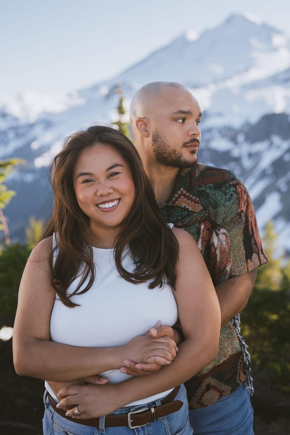 A romantic couple embraces against snowy mountain backdrop during golden hour outdoor photography session.