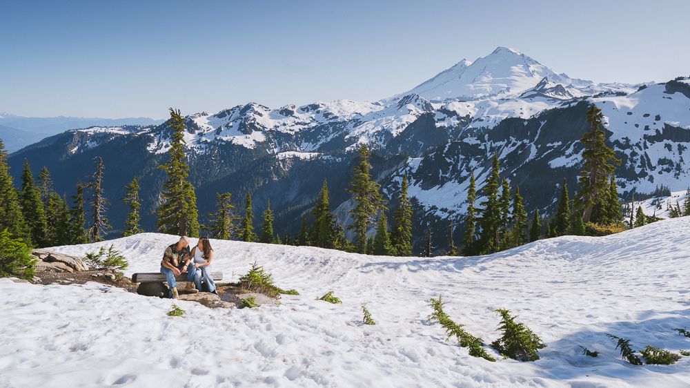 A snowboarder sits on a snowy slope overlooking Mount Baker's majestic peak in Washington State.