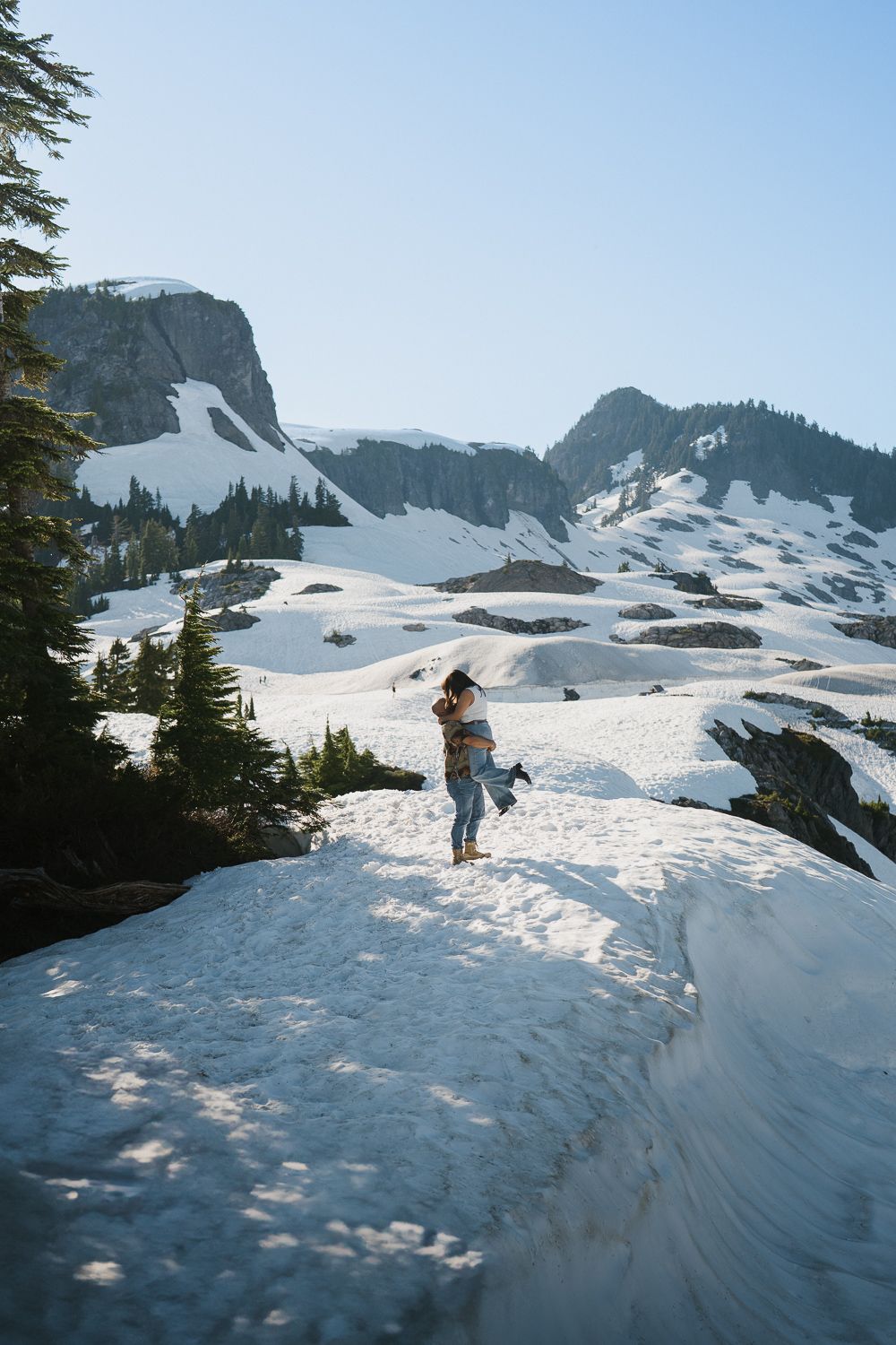 Winter adventurer stands on snowy mountain peak overlooking rugged alpine landscape in dramatic mountain setting.