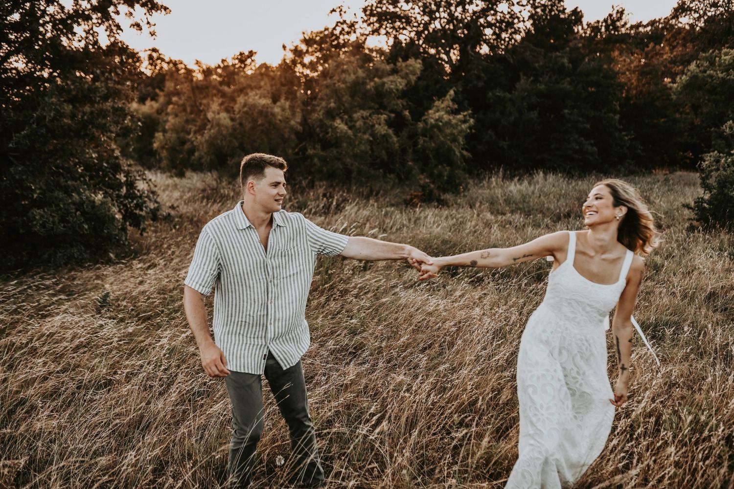 Engaged couple twirling playfully in a sunlit field during golden hour