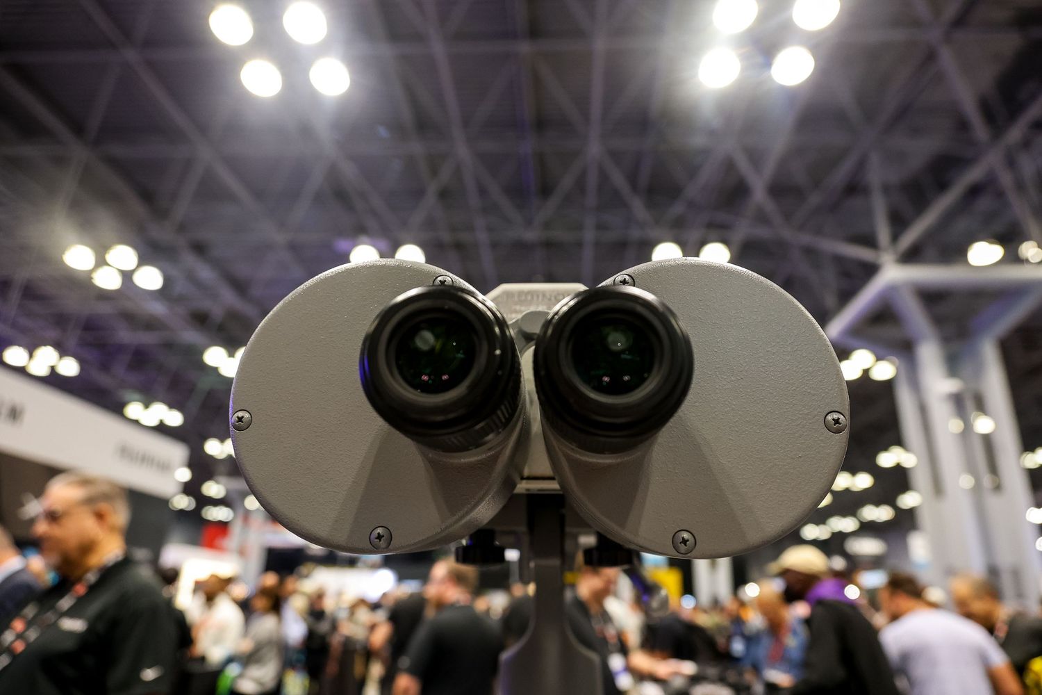 A series of microscope eyepieces lined up at a science exhibition with blurred crowd in background.
