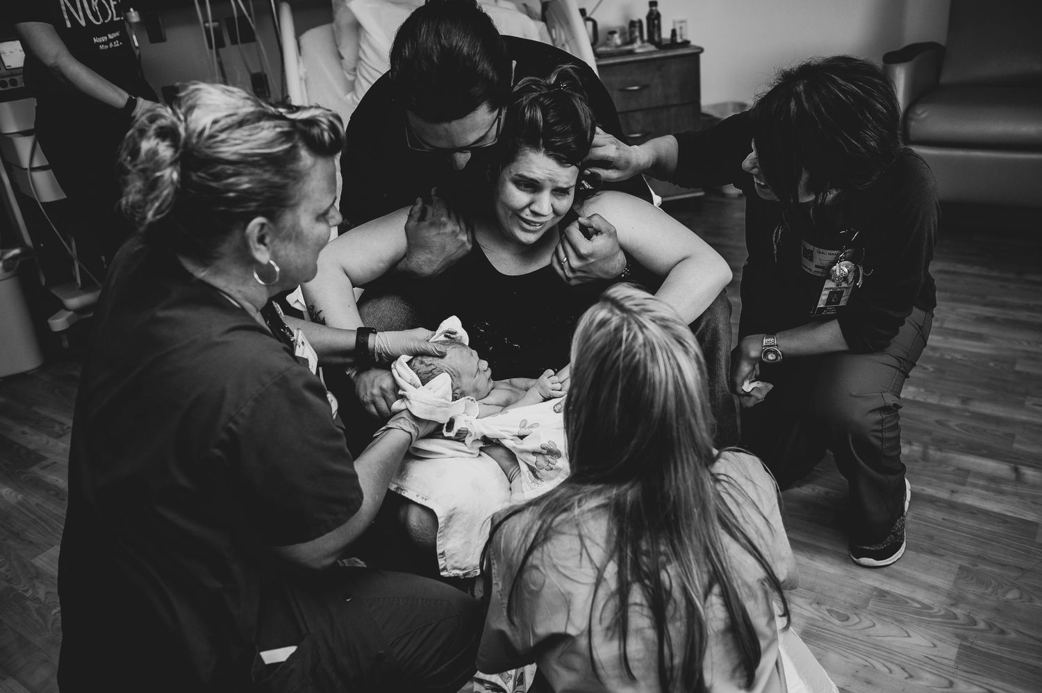 A candid black and white photo shows people gathering around a table in an intimate social setting.