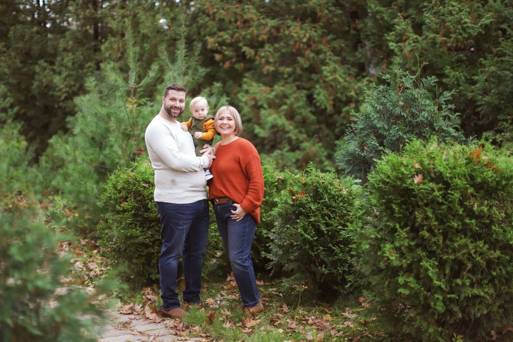A group poses together in front of green bushes and trees on a garden path during autumn.