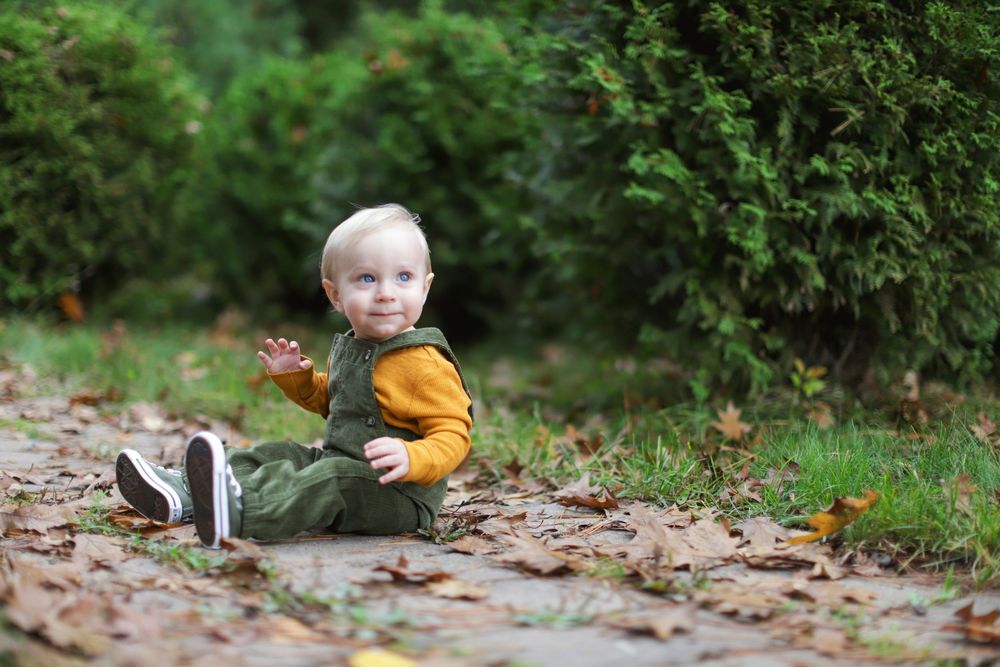 A person crouches in fallen autumn leaves while wearing a yellow sweater and playing outdoors.