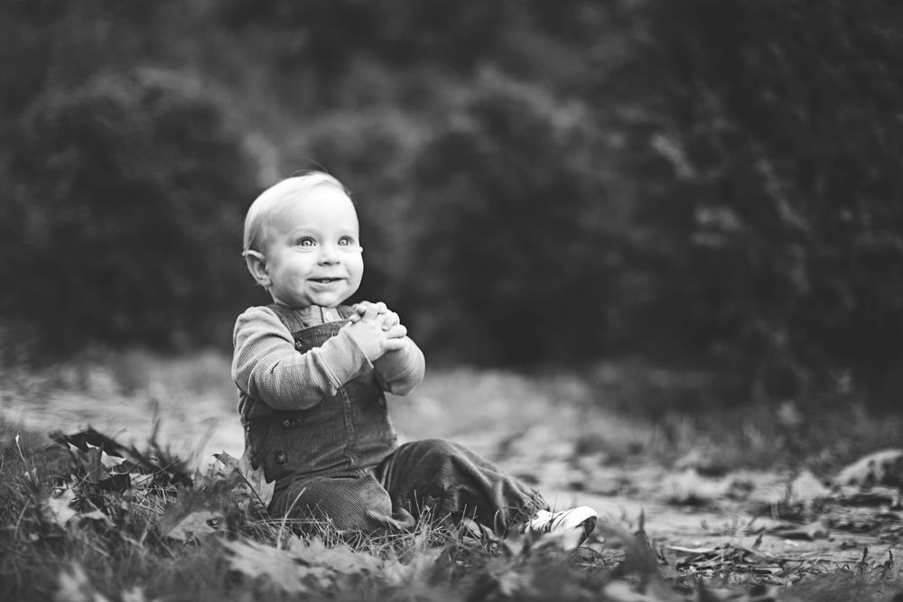 Black and white portrait of a joyful small child sitting outdoors amongst autumn leaves.