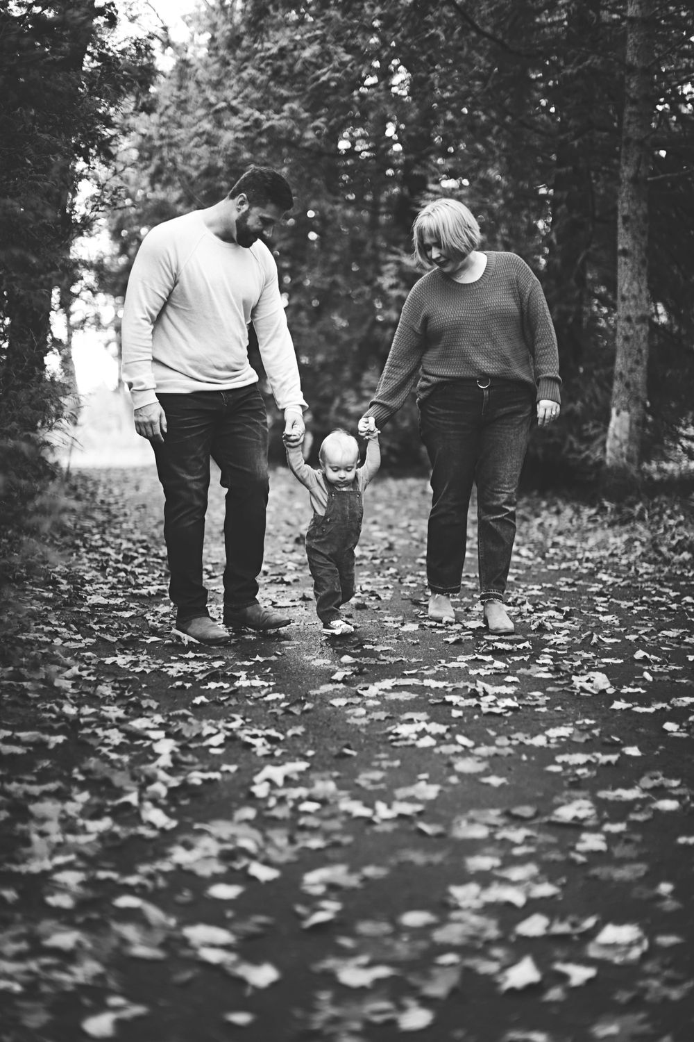 Low angle black and white view of people walking together through fallen autumn leaves on the ground.