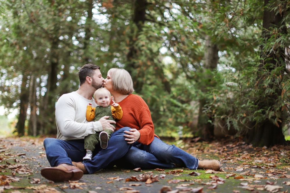 Family lying together on autumn leaves in wooded area during outdoor photo session.