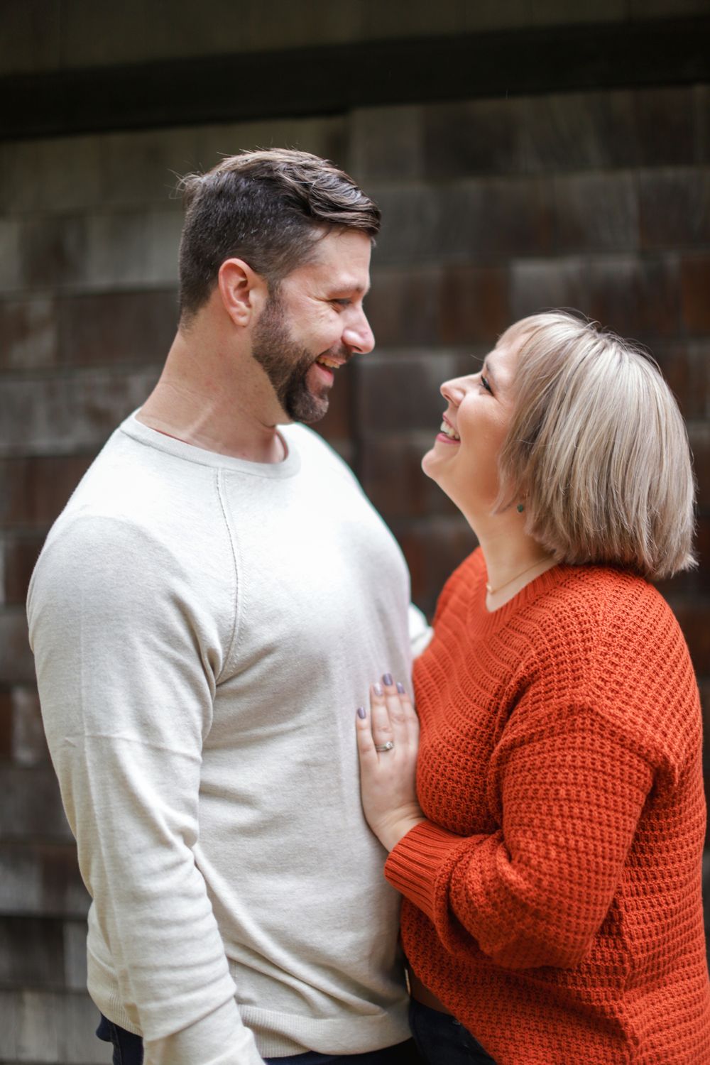 A couple shares a joyful moment together as they laugh while wearing casual knit sweaters against a dark background.