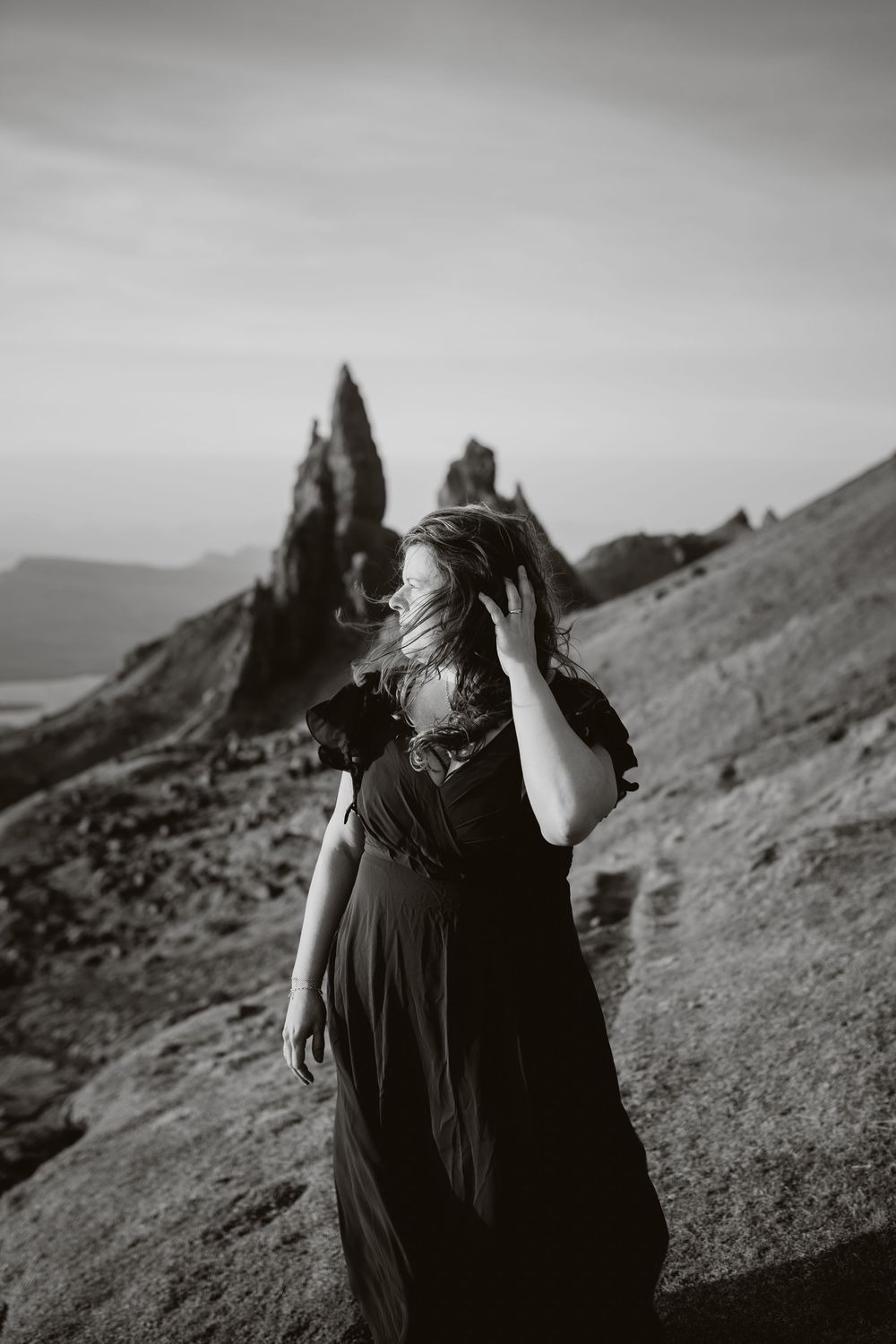 A black and white photo of a dark dress against a dramatic mountainous landscape with jagged rock formations.