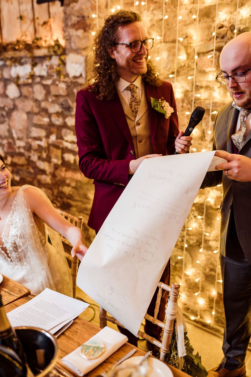 A wedding ceremony scene in a rustic stone venue with twinkling fairy lights on the wall.