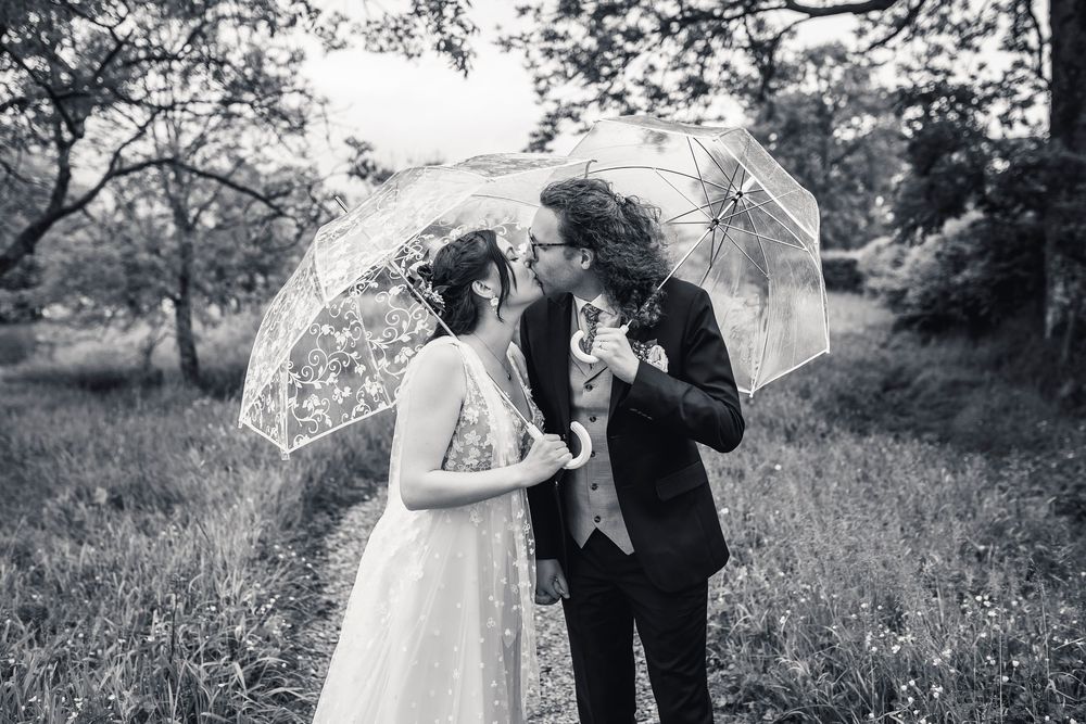 A black and white wedding photo of a couple sharing an intimate moment under a clear umbrella.