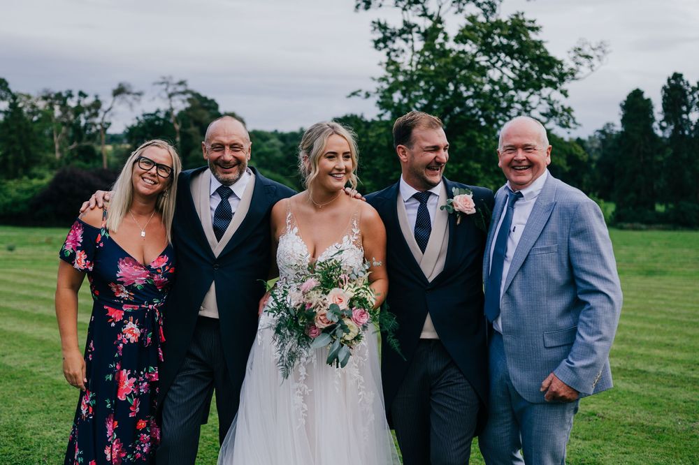 A group celebrating at an outdoor wedding ceremony on a lush green lawn with trees in the background.