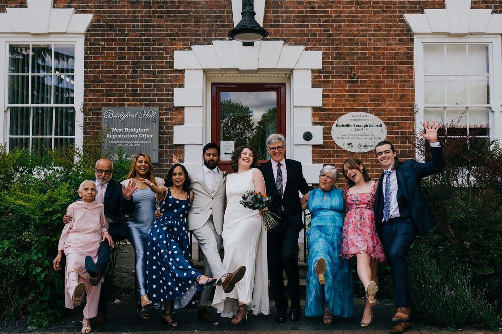 A wedding party poses together on the steps of a classic red brick building with white trim.