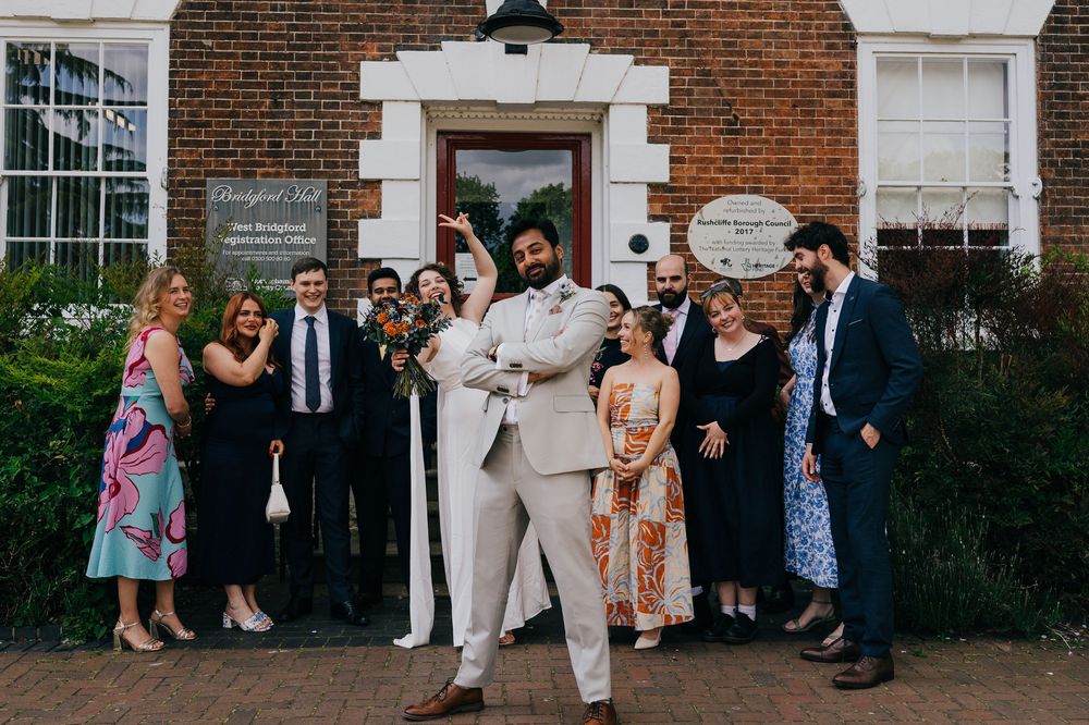 A group of stylishly dressed people pose together in front of a brick building entrance with white trim details.