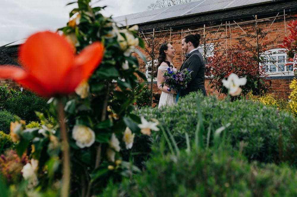 A couple celebrates their wedding moment in a garden with a vibrant red flower in the foreground.